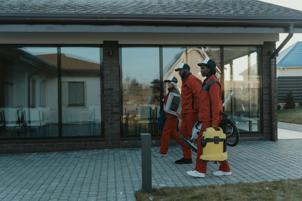 A professional cleaning team in uniforms with equipment approaching a glass-fronted house ready to perform a move in move out cleaning