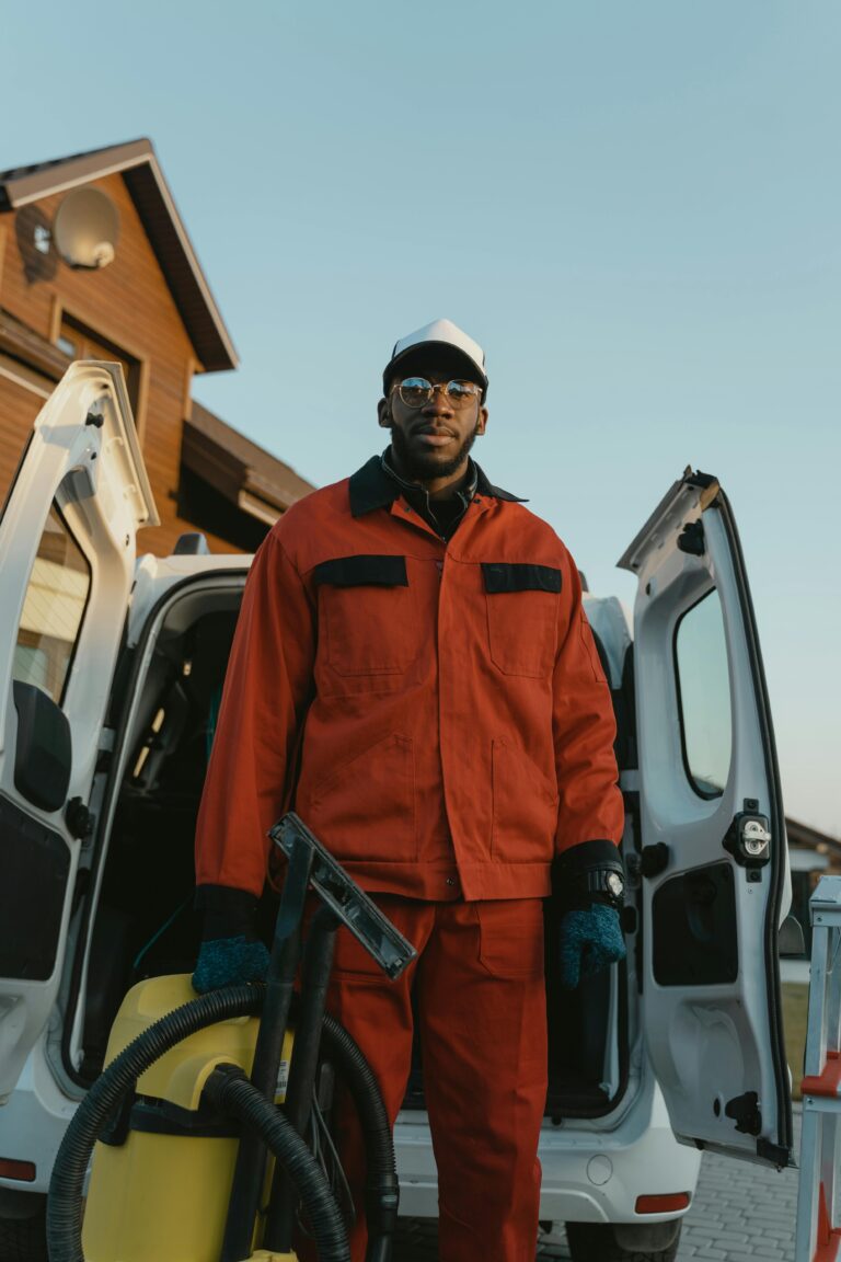 Man in work clothes with vacuum stands by a van in a residential area, showcasing post construction cleaning services.